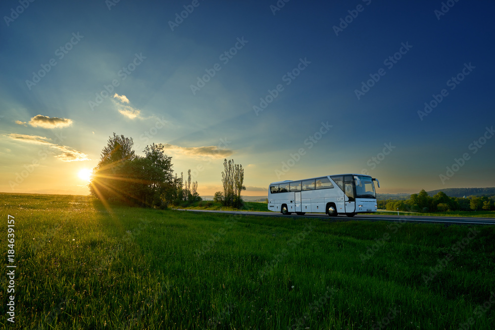 White bus traveling on the road in a rural landscape at sunset