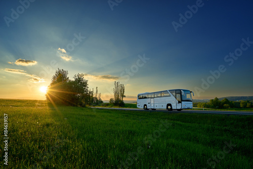 White bus traveling on the road in a rural landscape at sunset