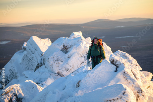Happy Woman hiker with backpack standing on the mountain peak abd smiling at cold winter day. Female hero and active lifestyle concept.