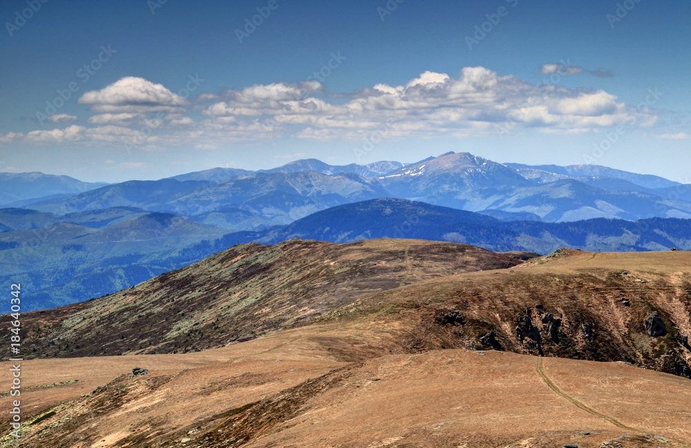 View of sunlit barren main ridge of Low Tatras towards Dumbier, highest peak of range, with white cumulus clouds in a sunny spring day from Kralova Hola peak, Low Tatra National Park, Slovakia, Europe
