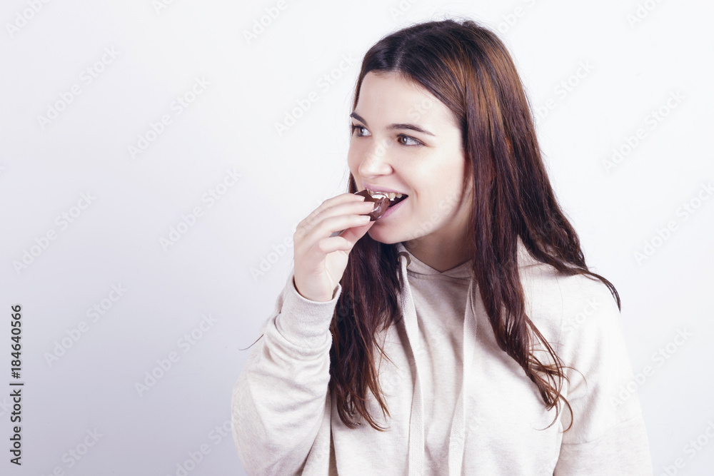 Young brunette girl eating a chocolate palm, a typical spanish bun. Indoors, over a grey wall. Young brunette girl eating a chocolate palm, a typical spanish bun. Indoors, over a grey wall.