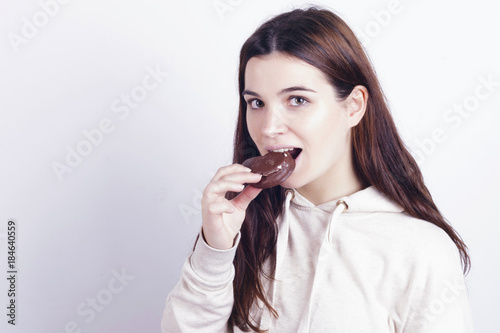 Young brunette girl eating a chocolate palm, a typical spanish bun. Indoors, over a grey wall.