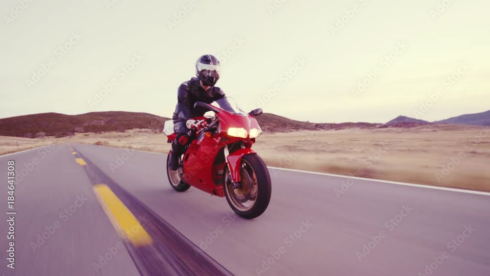 Motorcyclist racing his motorcycle down straight country road going a high speed at sunset Motorcyclist racing his motorcycle down straight country road going a high speed at sunset
