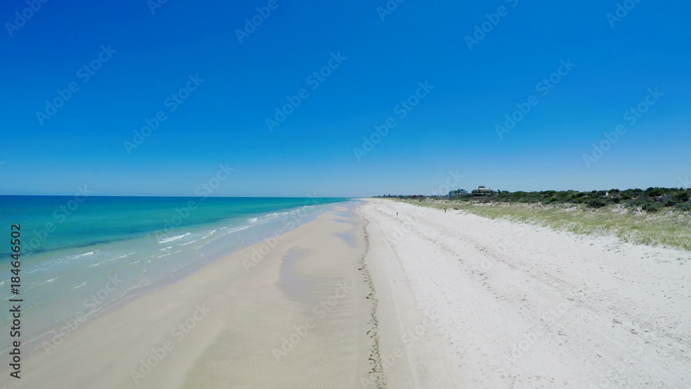 Drone aerial view of wide open white sandy beach, taken at Tennyson, South Australia with nearby luxury two story homes overlooking the coast.