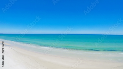 Drone aerial view of wide open white sandy beach, taken at Tennyson, South Australia with lone walker exercising, static.