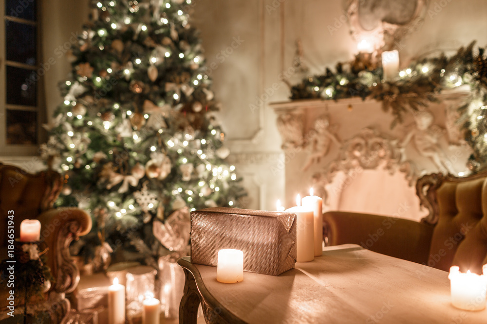 the gifts on the table. Christmas evening by candlelight. classic apartments with a white fireplace, decorated tree, sofa, large windows and chandelier.