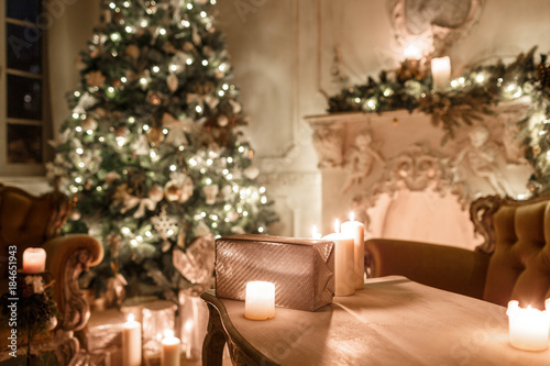 the gifts on the table. Christmas evening by candlelight. classic apartments with a white fireplace  decorated tree  sofa  large windows and chandelier.