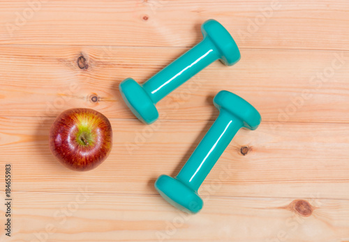 Two green dumbbells and apple on wooden background