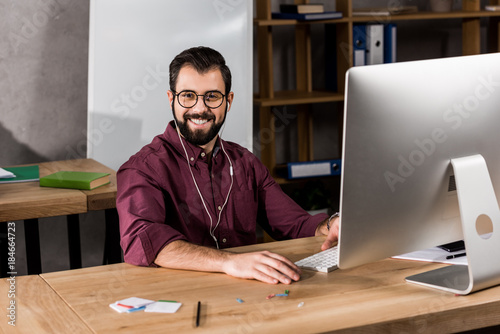 smiling businessman working at computer in office and looking at camera