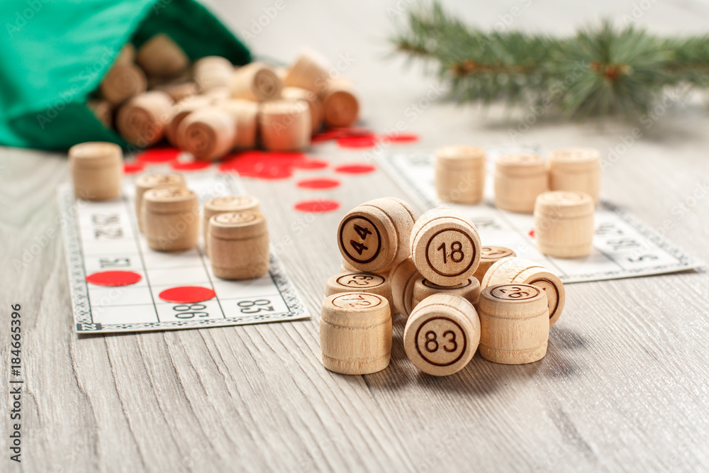 Wooden lotto barrels with bag, game cards and red chips for a game in lotto, Christmas fir tree branches Wooden lotto barrels with bag, game cards and red chips for a game in lotto, Christmas fir tree branches