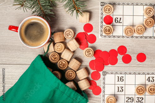 Wooden lotto barrels with bag, game cards, red chips and cup of coffee, Christmas fir tree branches