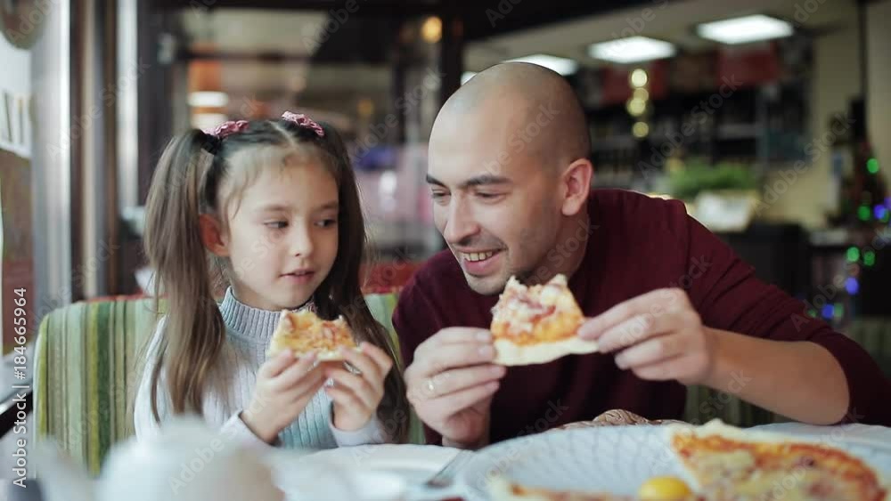 Dad with a small daughter eat pizza at a pizzeria. Unhealthy food, Eating fast food Dad with a small daughter eat pizza at a pizzeria. Unhealthy food, Eating fast food