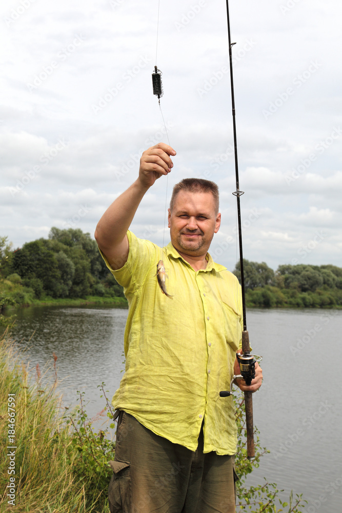 The fisherman caught a small fish on a fishing trip in the summer. A happy  man during a holiday in nature. Perch - an excellent catch on the river.  Stock Photo