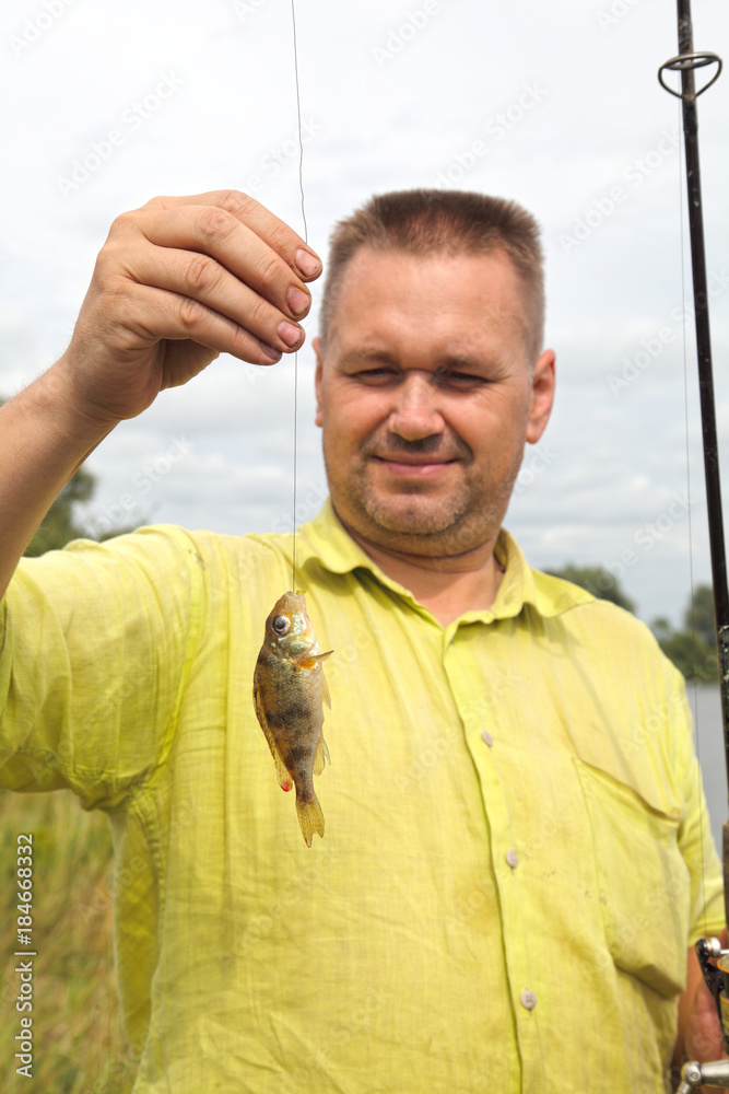 The fisherman caught a small fish on a fishing trip in the summer. A happy  man during a holiday in nature. Perch - an excellent catch on the river.  Stock Photo