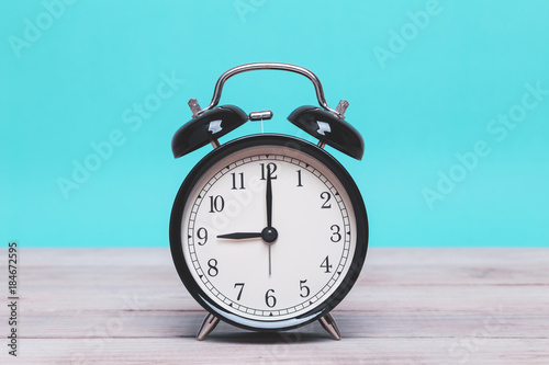 A Black Retro alarm clock on wooden board with green background