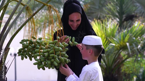 Arabic mother and son touching dates on tree.