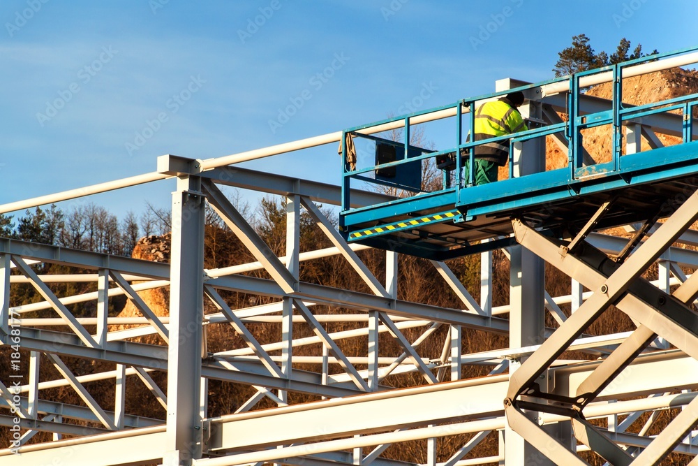 Naklejka premium The steel structure is under construction. Installation of metal halls. Work at height. A sunny day at a construction site.