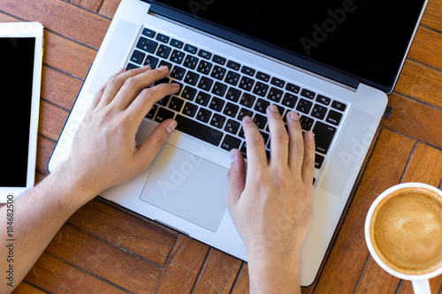 Young man hands working on laptop computer placed on wooden desk. Top view