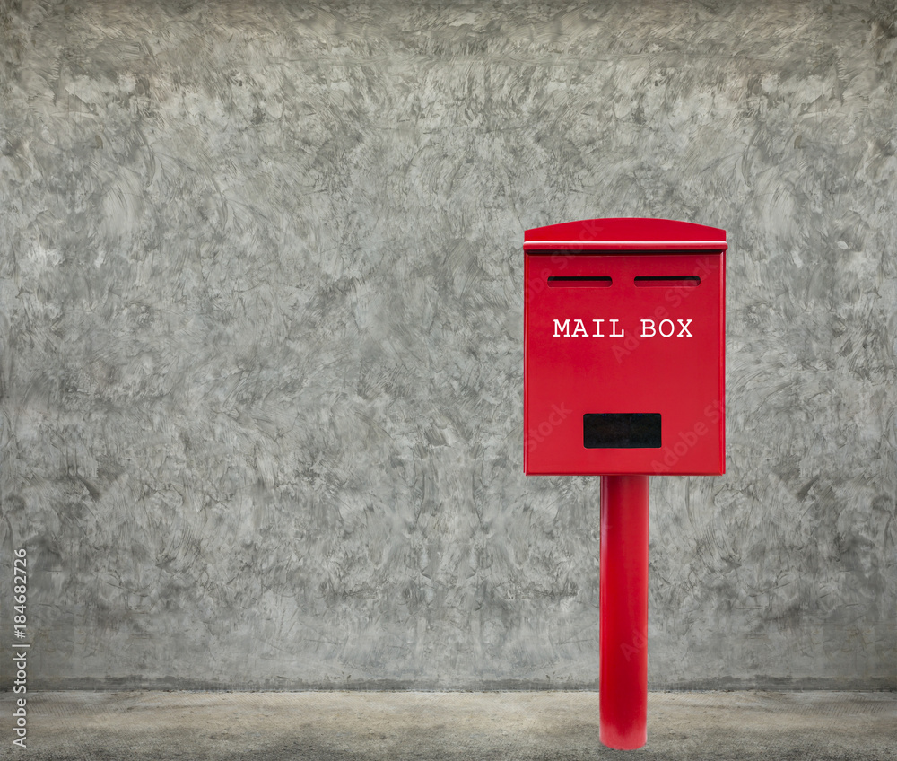Red mail box on cement floor with cement wall as background