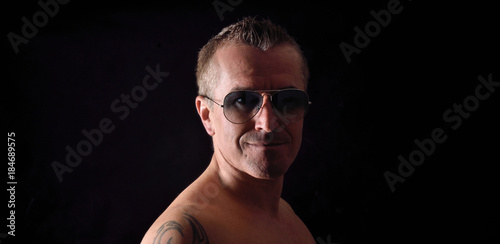 portrait of a man with tattoo and sunglasses and black background