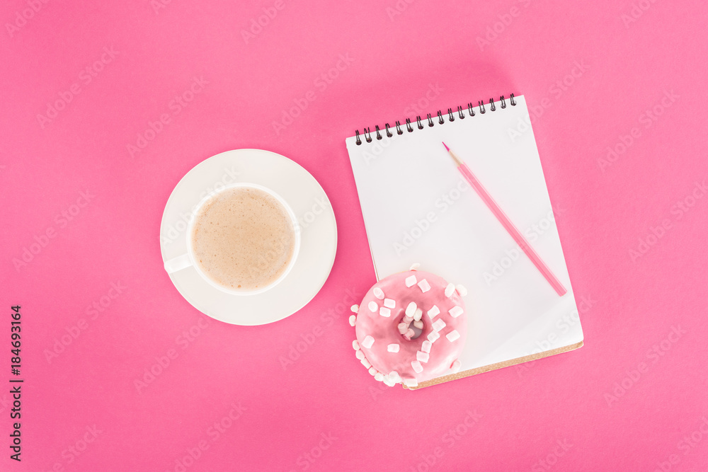 top view of glazed doughnut with cup of coffee and blank notebook on pink surface top view of glazed doughnut with cup of coffee and blank notebook on pink surface