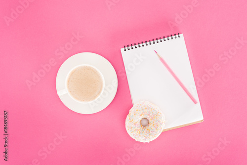 top view of glazed doughnut with cup of coffee and blank notebook