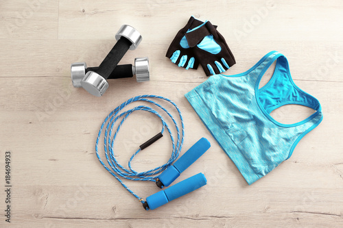 Jumping rope, sport top, dumbbells and gloves on wooden background