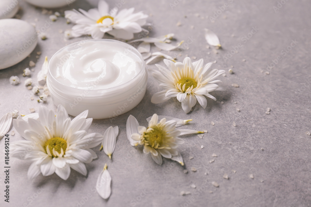 Jar of body cream and flowers on grey background Jar of body cream and flowers on grey background