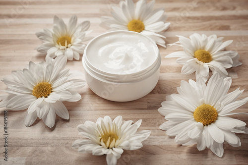 Jar of body cream and flowers on wooden background