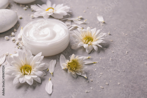 Jar of body cream and flowers on grey background