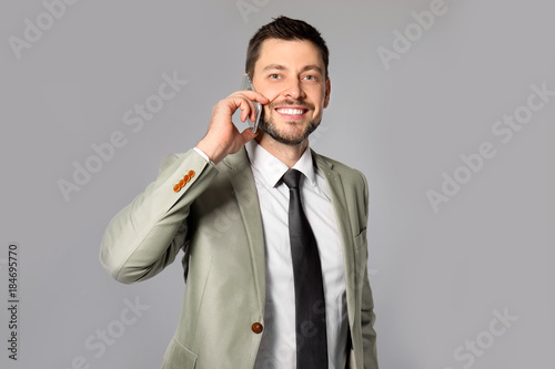 Attractive businessman talking on phone against grey background
