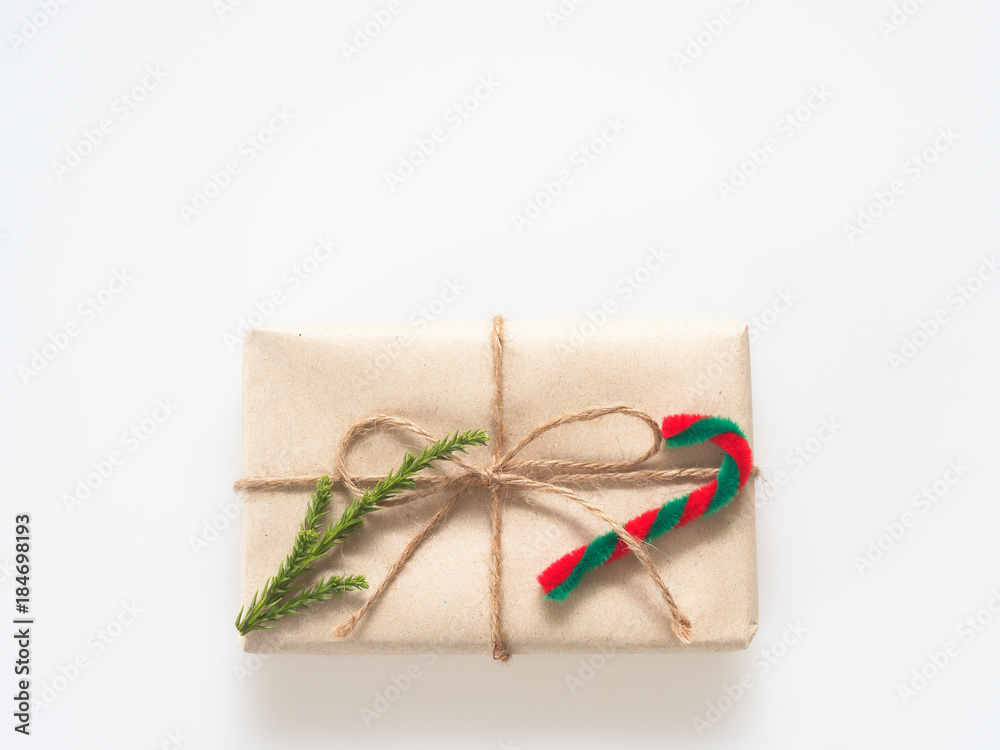 A present or gift box wrapped by rough brown recycled paper and tied with brown hemp rope ribbon with pine branch and candy cane isolated on white background with green and eco freindly concept