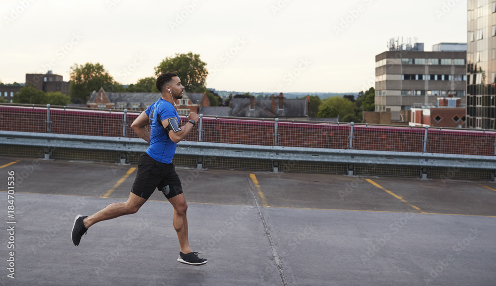 Young male athlete running on a road, side view