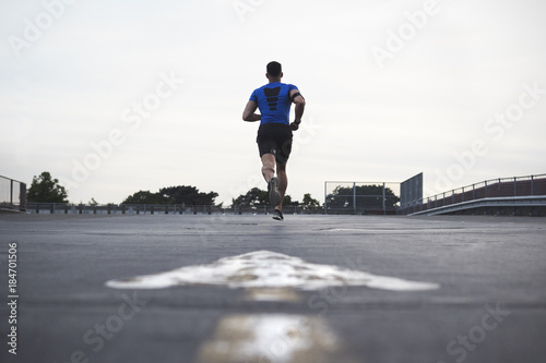 Male athlete running on a road away from camera, full length