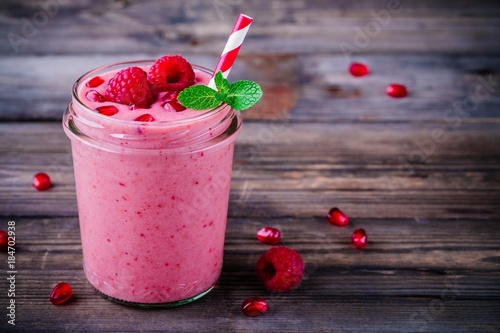 Pink pomegranate smoothie in a glass jar with mint and fresh raspberries