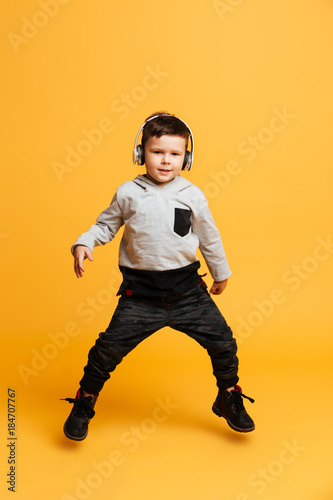 Boy child standing isolated listening music with headphones.