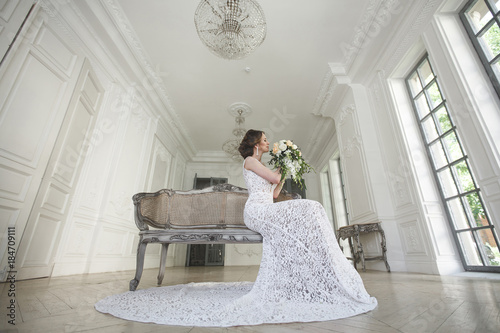 Beautiful bride posing in wedding dress in a white photo Studio. Mirror. Sofa. Bouquet. The door. Chandelier.