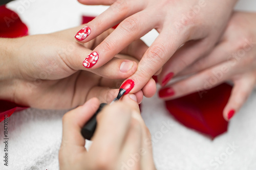 Manicure. Closeup Of Beautiful Woman Hands Polishing Nails With Red Nail Polish In Beauty Salon. Close-up Of Beautician Hand Painting Female Client Nails. Beauty Concept. High Resolution