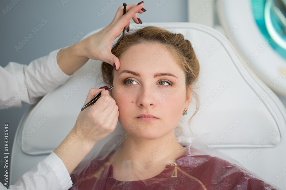 Fototapeta premium Tweezing eyebrow by beautician. Isolated.