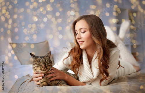 happy young woman with cat lying in bed at home