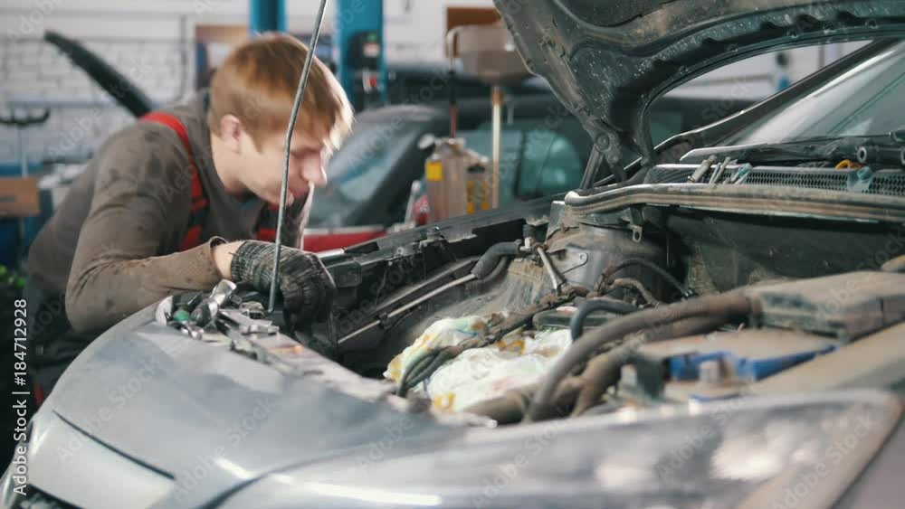 Mechanic checks automobile engine, car repair, working in the workshop, overhaul, under the hood Mechanic checks automobile engine, car repair, working in the workshop, overhaul, under the hood