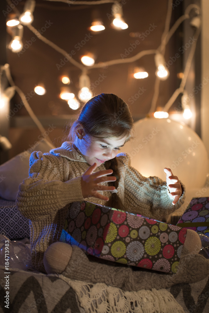 Beautiful little girl opens a magical Christmas gift in the cozy interior of the house. New year.