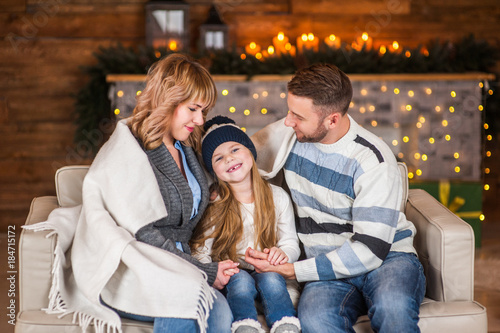 Family of mother, father and little child daughter near Christmas tree and fireplace with presents, decorations and New Year or Christmas © Анна Ковальчук