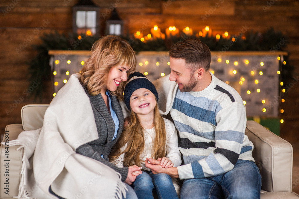 Family of mother, father and little child daughter near Christmas tree and fireplace with presents, decorations and New Year or Christmas