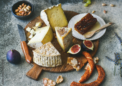 Cheese platter with cheese assortment, figs, honey, freshly baked bread and nuts on wooden board over grey concrete background. Party or gathering eating concept