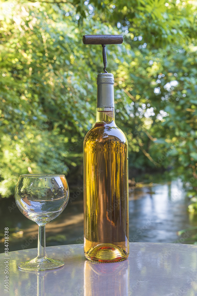 Obraz premium bottle of white wine/bottle of white wine with corkscrew on a table in the park with the river