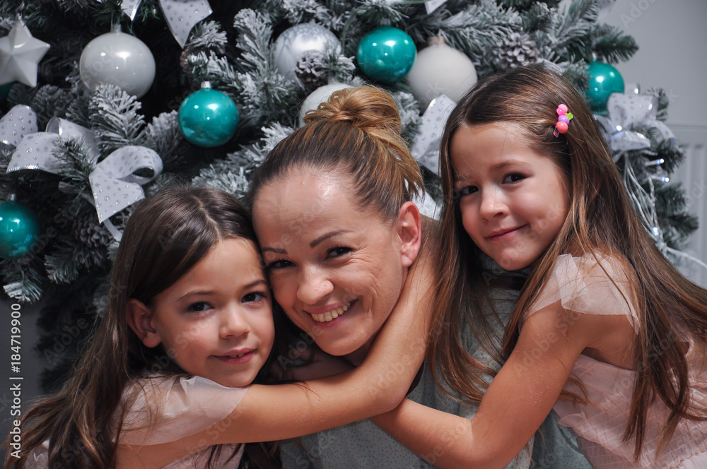 Two little girls hugging their mom. Smiling daughters hugging mom for Christmas