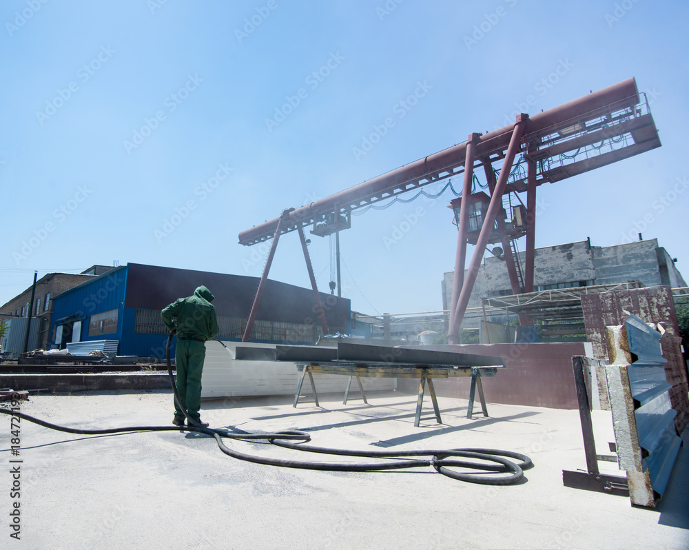 Fototapeta premium factory for cleaning of metal by sandblasting. a worker cleans the metal by sandblasting