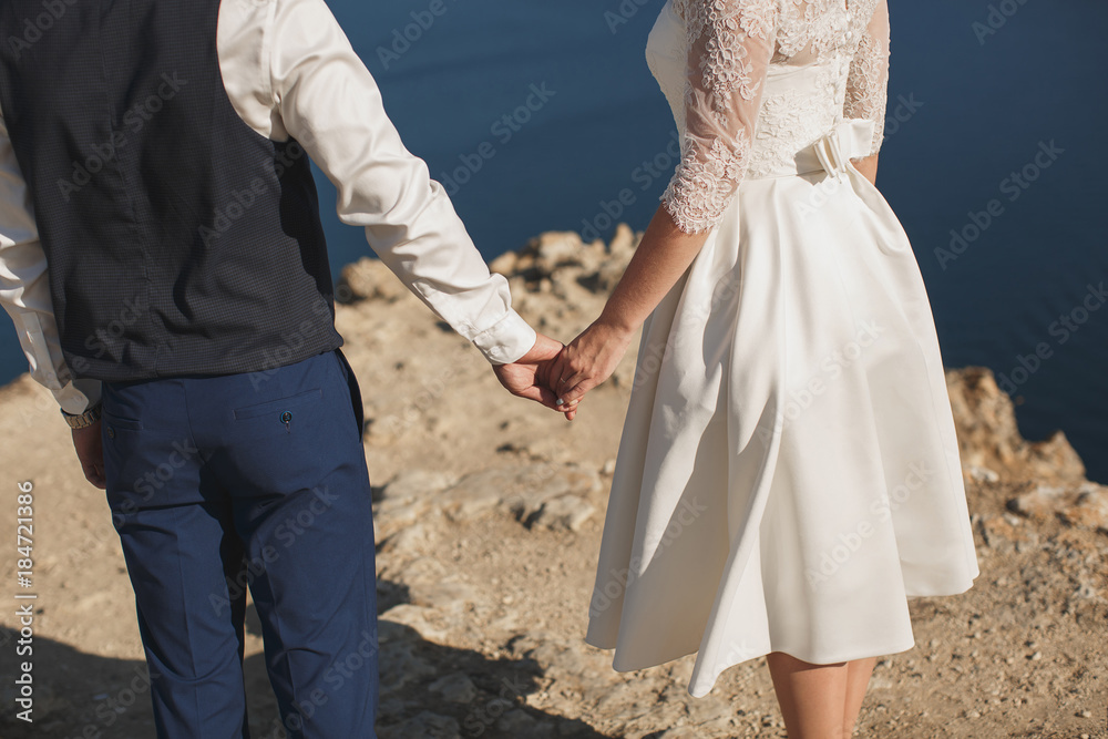 Bride and groom walking together holding their hands. Mountain. Sea. Ocean. Bride and groom walking together holding their hands. Mountain. Sea. Ocean.