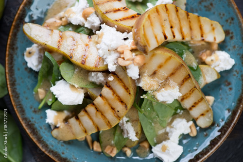 Salad with fresh spinach leaves, grilled pear slices, feta cheese and nuts, view from above, close-up